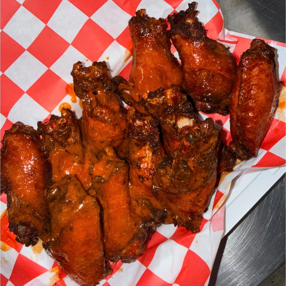 Glazed, crispy chicken wings and drumsticks arranged on red-and-white checkered food paper.