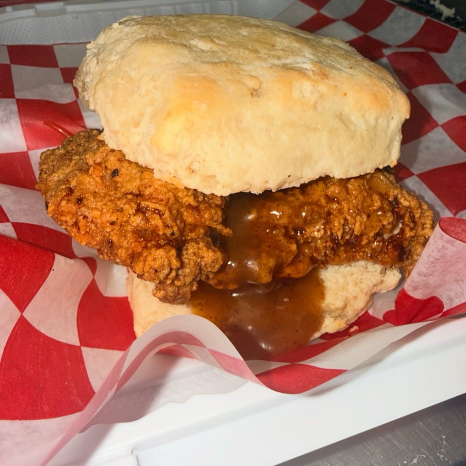 Crispy fried chicken sandwich with brown gravy on a biscuit, served in a red-and-white checkered basket liner.